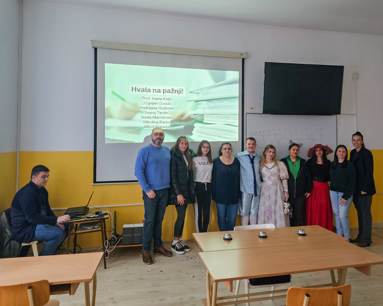 A group of people standing in a room with a projector screen

Description automatically generated
